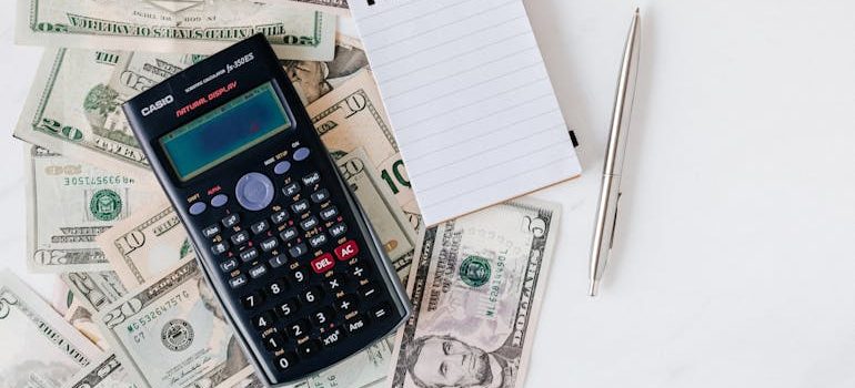 Calculator and Notepad placed over Stack of Paper Bills