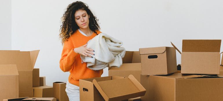 Focused young relocating female packing belonging into cardboard boxes